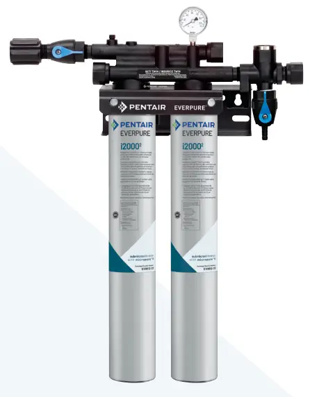 A dual-cartridge water filtration system with two long white cartridges attached to a black manifold with a pressure gauge.